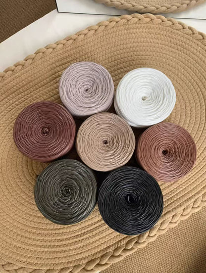 A vibrant flat lay arrangement of multiple cakes of premium matte satin faux leather ribbon yarn. The various cakes display a rich and harmonious color palette, including muted metallics, jewel tones, and neutrals such as a dusty rose, sage green, deep teal, copper bronze, slate gray, olive, matte black, pure white, and soft silver gray, showcasing the smooth, durable texture and uniform color.