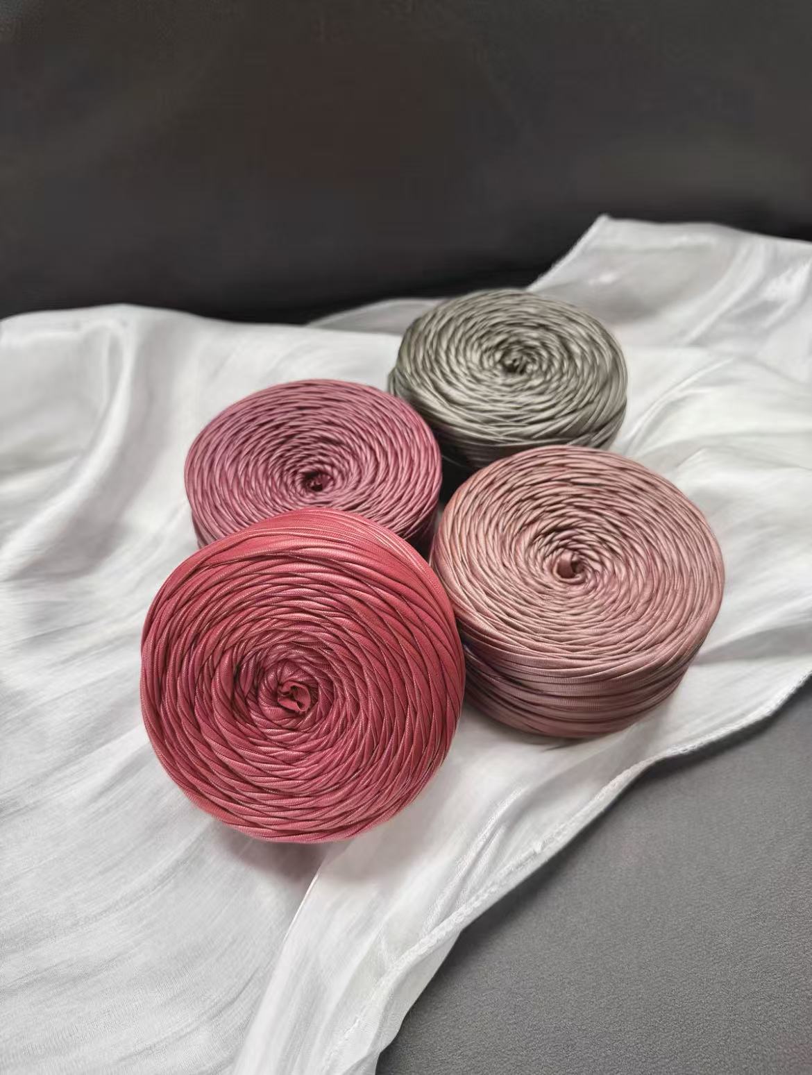 A vibrant flat lay arrangement of multiple cakes of premium matte satin faux leather ribbon yarn. The various cakes display a rich and harmonious color palette, including muted metallics, jewel tones, and neutrals such as a dusty rose, sage green, deep teal, copper bronze, slate gray, olive, matte black, pure white, and soft silver gray, showcasing the smooth, durable texture and uniform color.