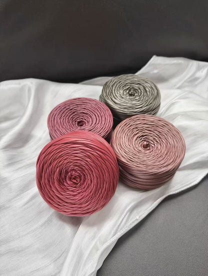 A vibrant flat lay arrangement of multiple cakes of premium matte satin faux leather ribbon yarn. The various cakes display a rich and harmonious color palette, including muted metallics, jewel tones, and neutrals such as a dusty rose, sage green, deep teal, copper bronze, slate gray, olive, matte black, pure white, and soft silver gray, showcasing the smooth, durable texture and uniform color.